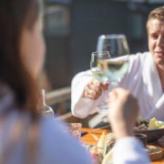 Un couple en peignoir trinque avec du vin en mangeant au soleil.